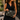 Woman in a black dress on a city street holding the Chestnut Lovebug Clutch by Hadley Pollet with cream flowers and beetles