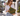 Woman in a white shirt and jeans on a palm-lined street holding the Olive Lovebug Clutch by Hadley Pollet